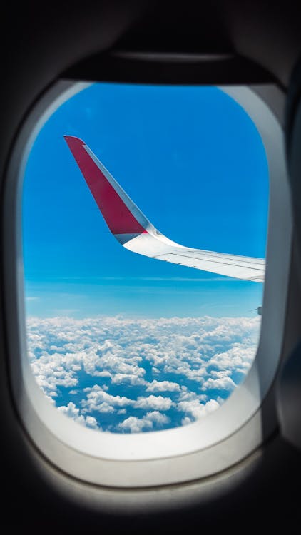 An airplane window with the sky and clouds in the background