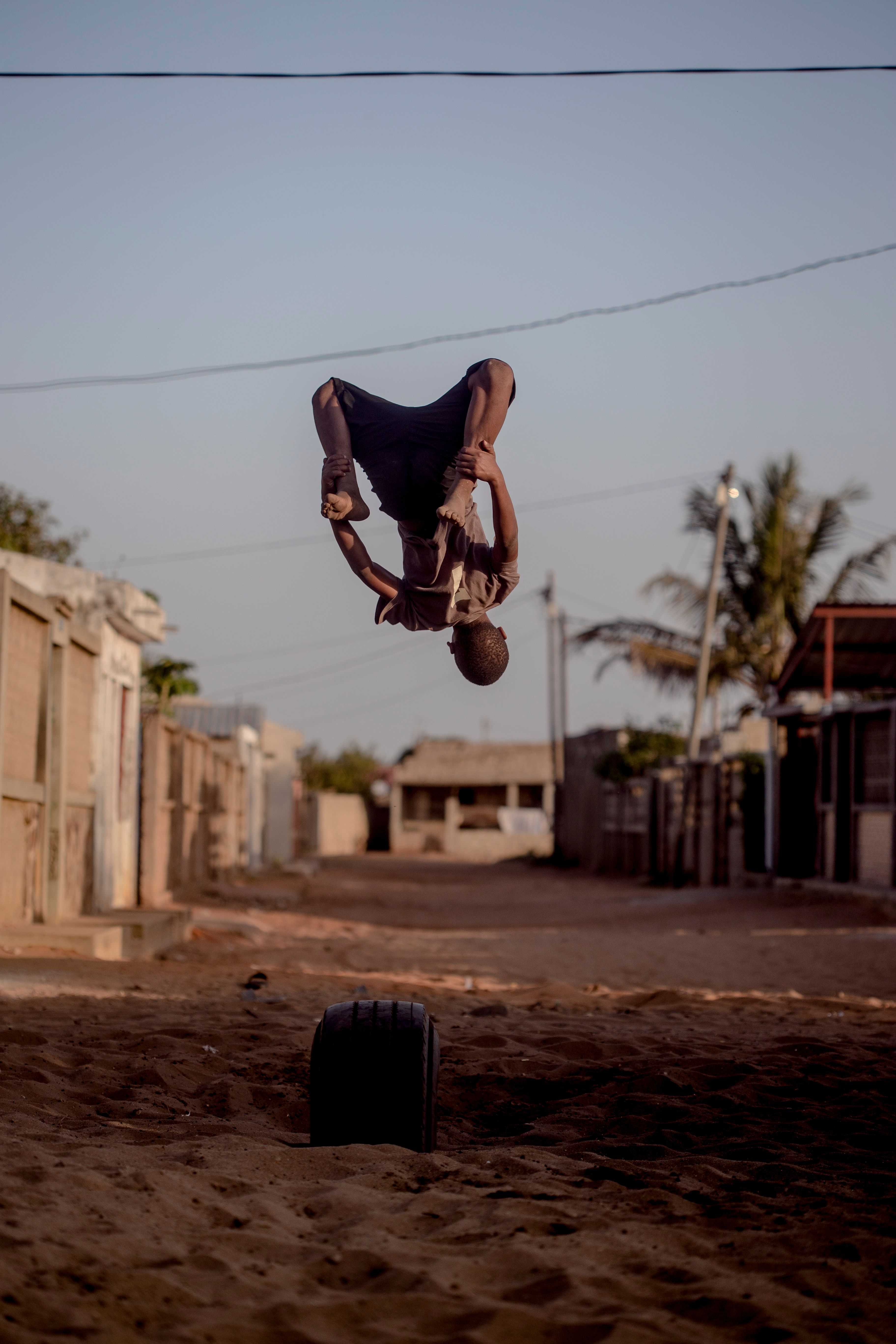 A young man executes an acrobatic flip in a sandy urban street in Maputo, Mozambique.