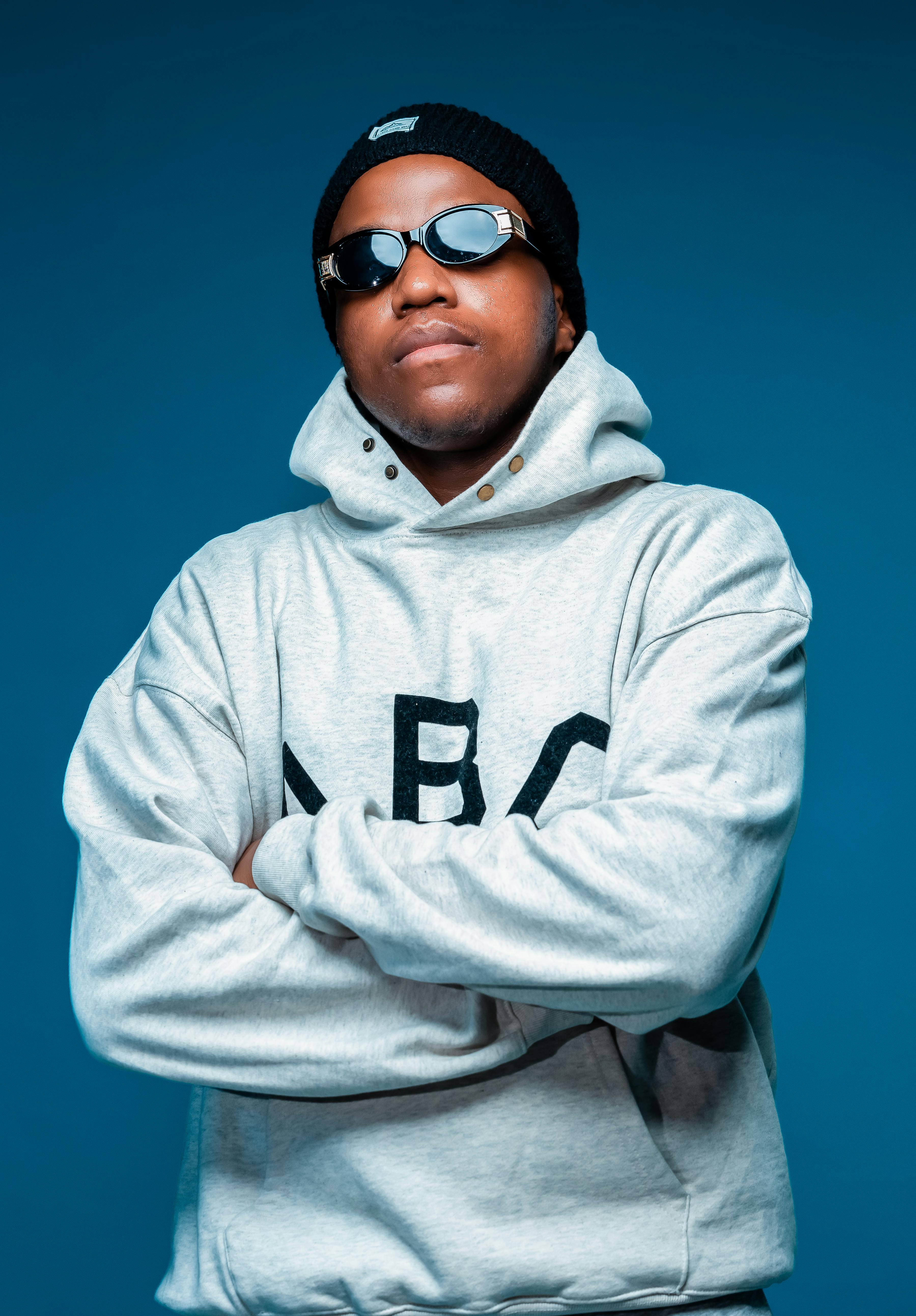 Stylish man wearing a hoodie and sunglasses against a blue background. Studio shoot in Montreal.