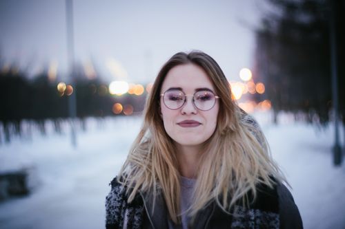 Free A young woman with eyeglasses and blonde hair posing outdoors in a winter setting. Stock Photo