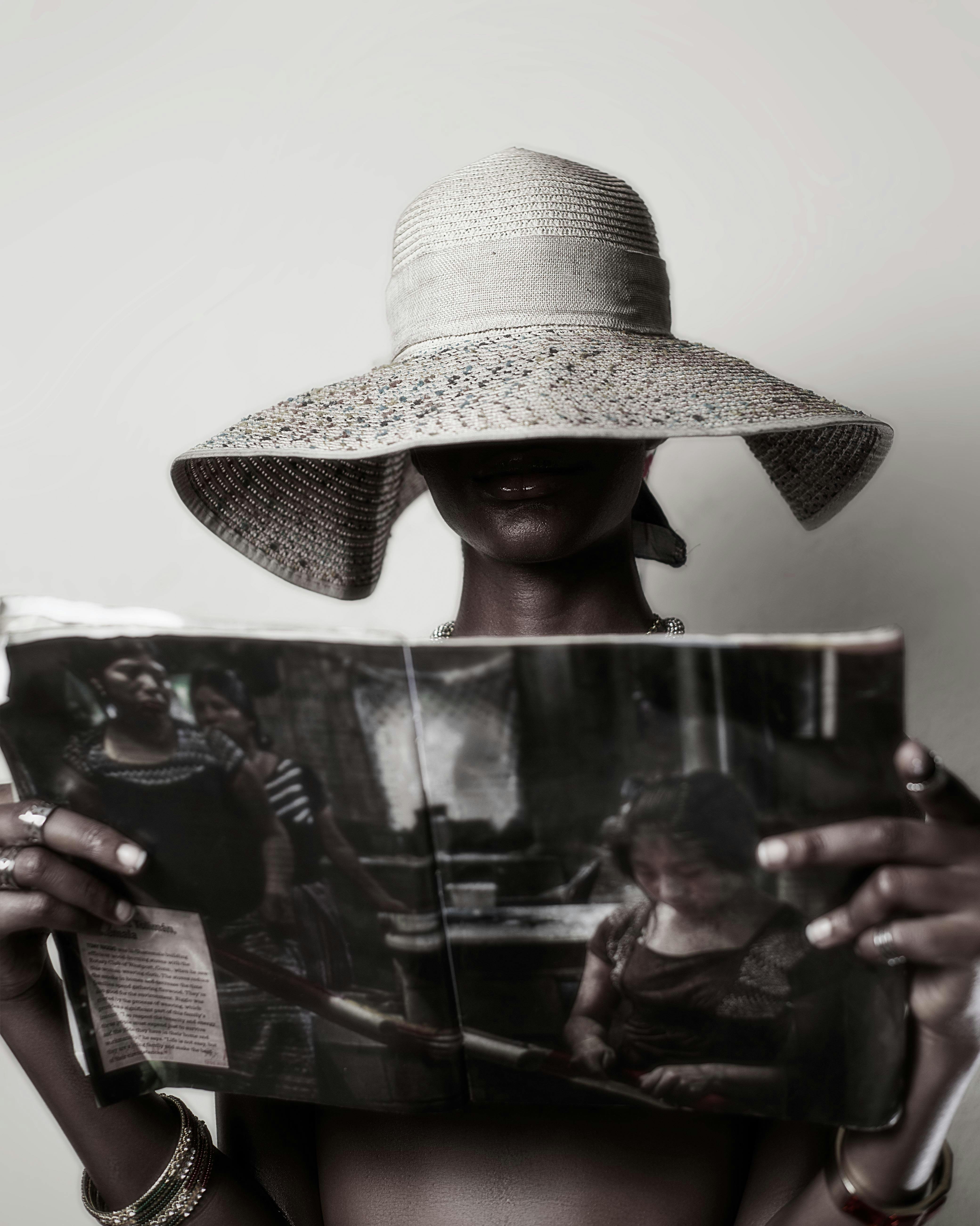 woman in a hat covering the half of her face holding and looking at a magazine