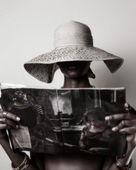 A stylish woman in a hat reads a magazine with focus on elegance and fashion.