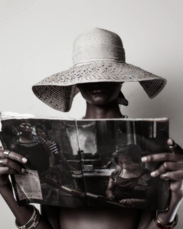 Woman in a Hat Covering the Half of Her Face Holding and Looking at a Magazine 