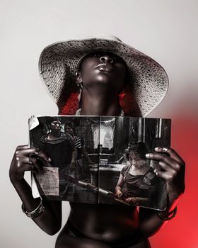 Stylish portrait of a woman in a wide-brimmed hat holding an open magazine.