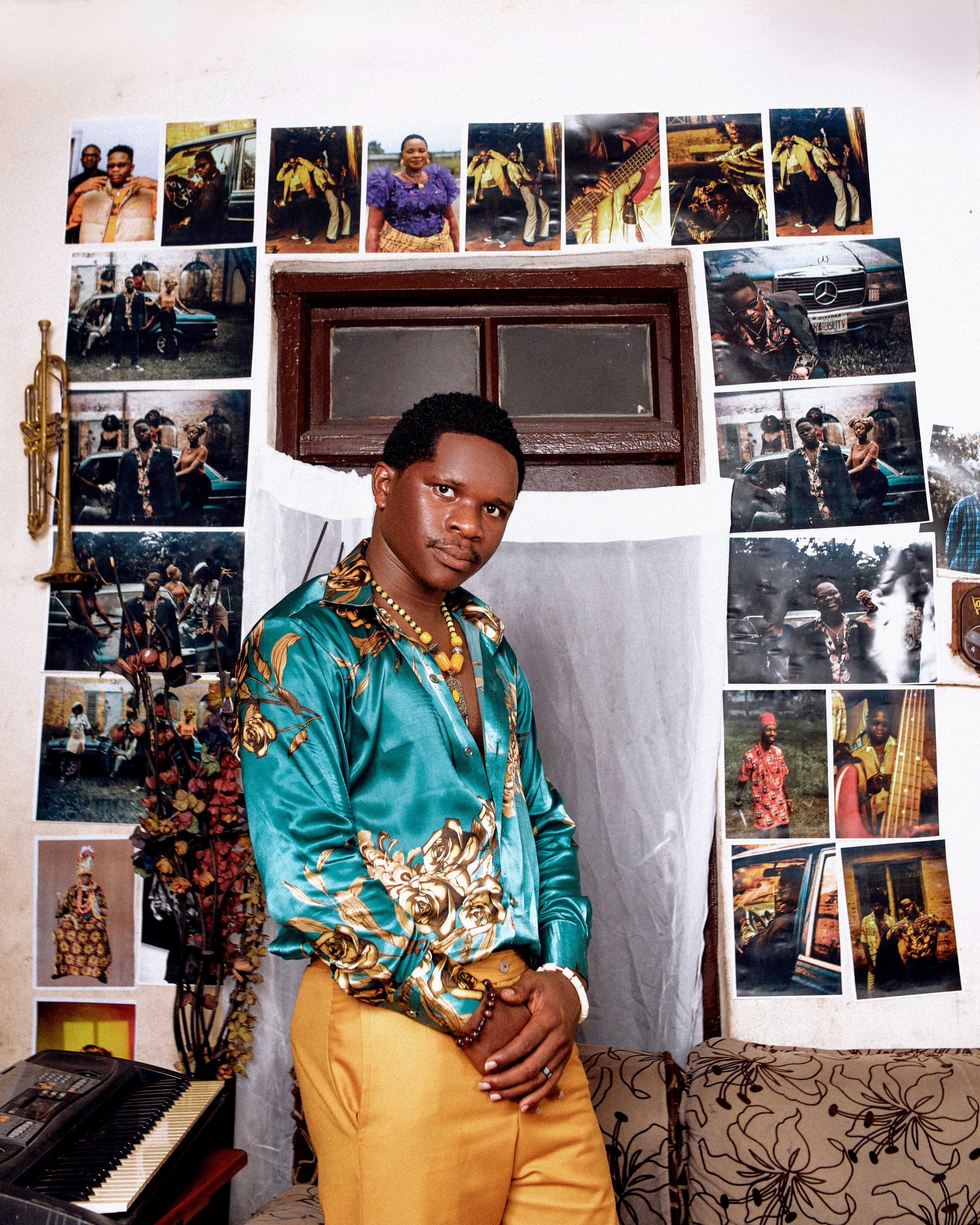 A fashionable man poses confidently in a vibrant room filled with photographs, showcasing unique style.