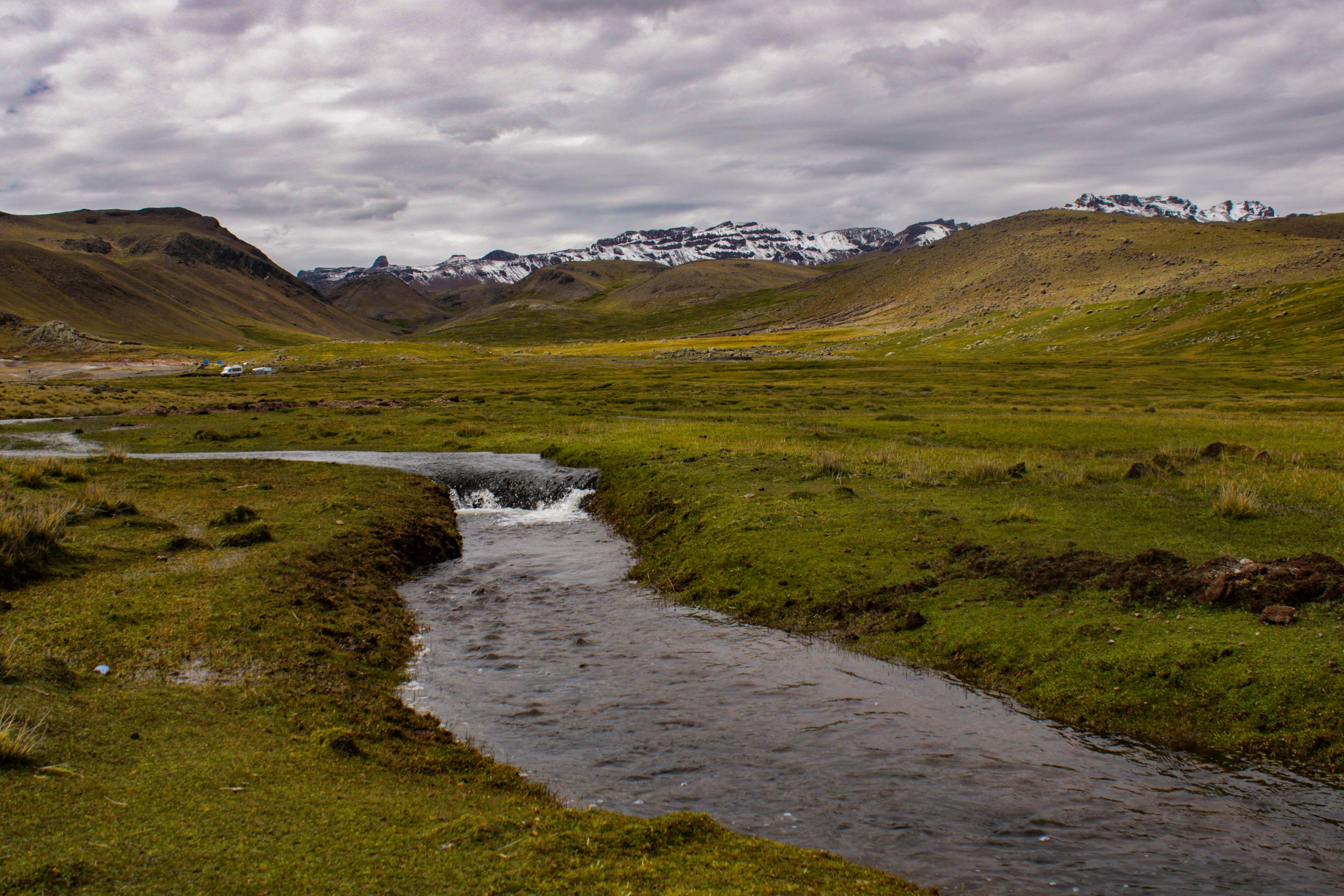A stream runs through a grassy field with mountains in the background ...