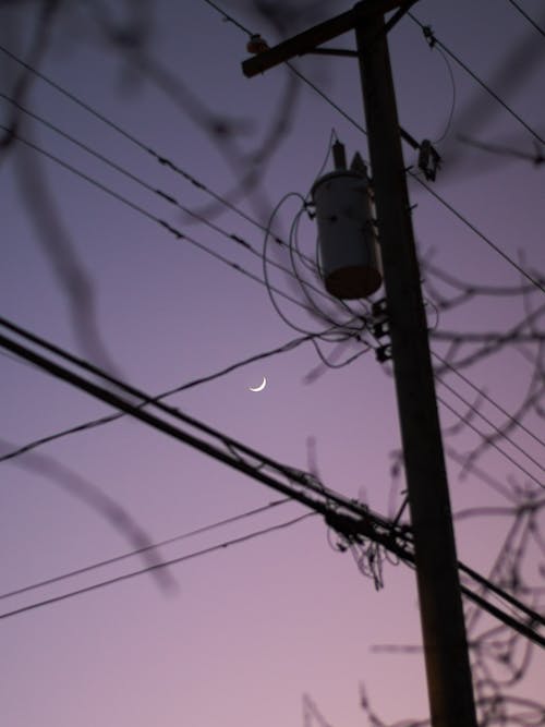 A crescent moon is seen in the sky over telephone wires