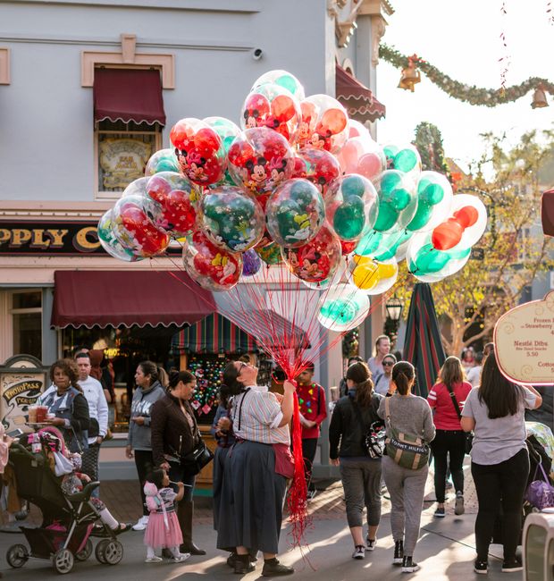 A lively street scene featuring a vendor selling vibrant balloons amidst a bustling crowd during daytime festivities.