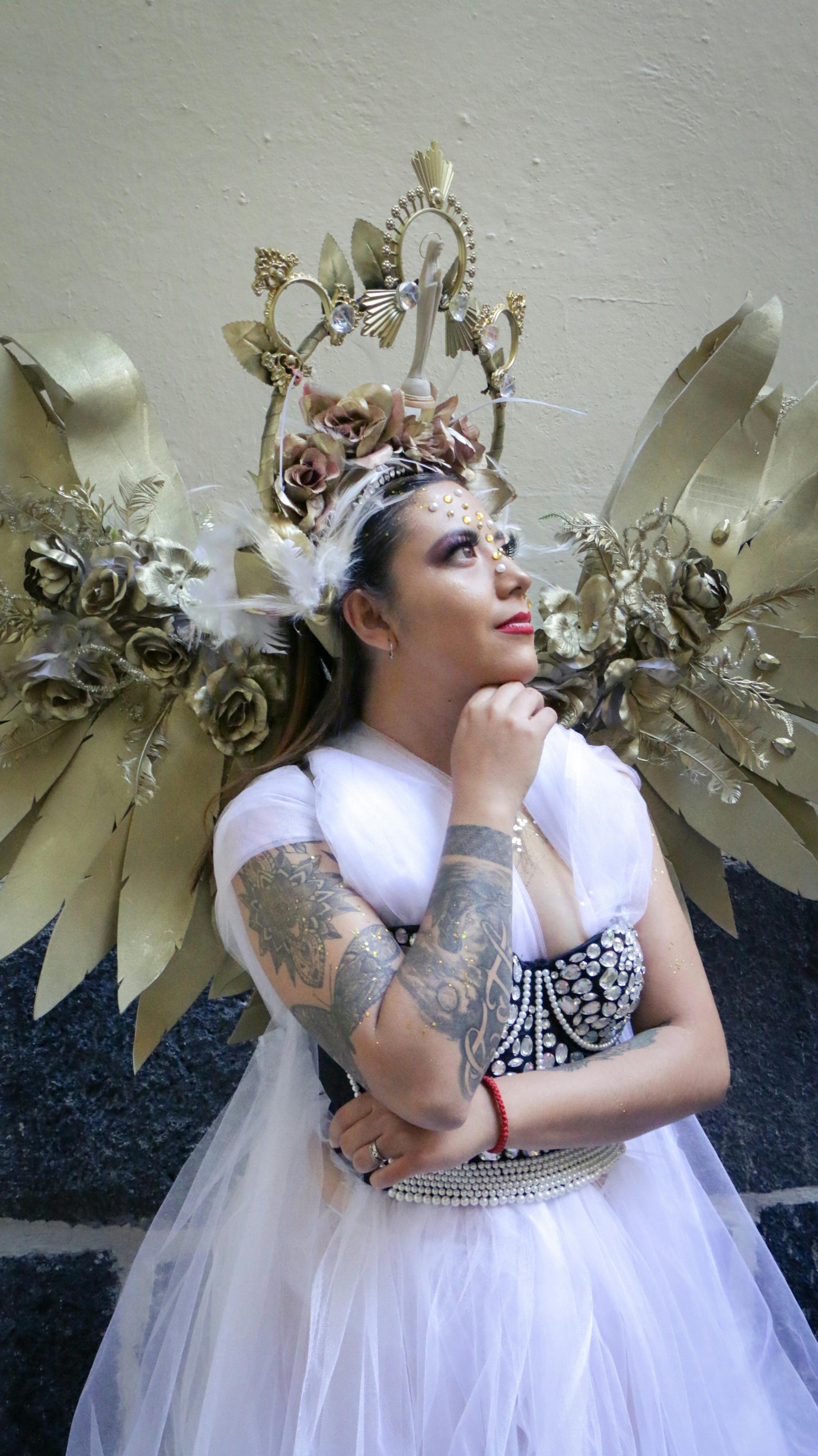 A woman in a white dress and golden wings posing elegantly indoors with ornate details.