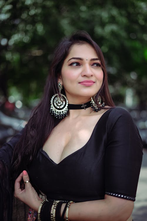 Photo of a Woman Wearing a Black Dress and Jewellery in a Park
