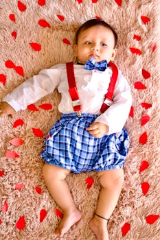 Adorable baby in stylish outfit with red suspenders and bowtie, surrounded by colorful decor.