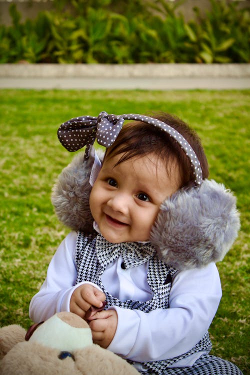 Baby Wearing Earmuffs, Sitting on a Green Lawn