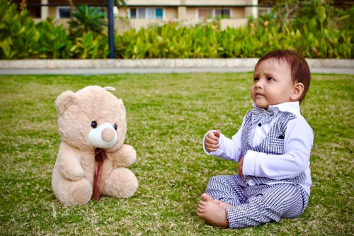 Free Baby Boy Sitting with a Teddy Bear on a Lawn Stock Photo