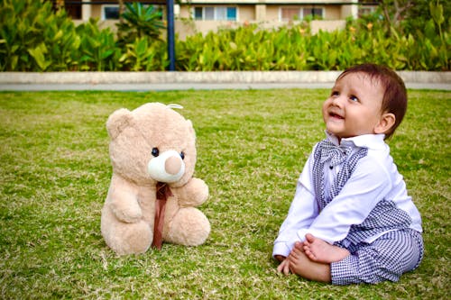 Free Baby Boy Sitting with a Teddy Bear on a Lawn Stock Photo