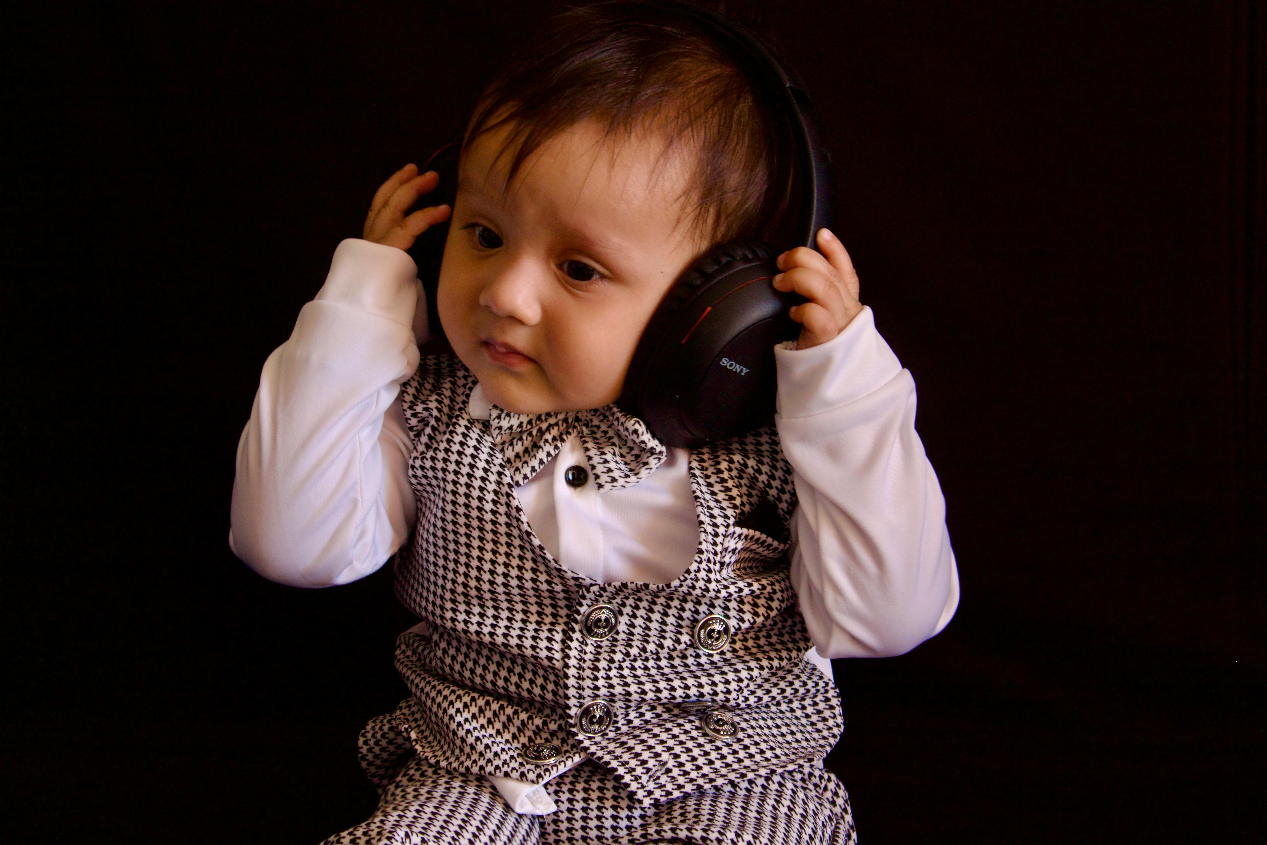 Cute baby in a checked vest and headphones, demonstrating early interest in music. Perfect for lifestyle and fashion imagery.