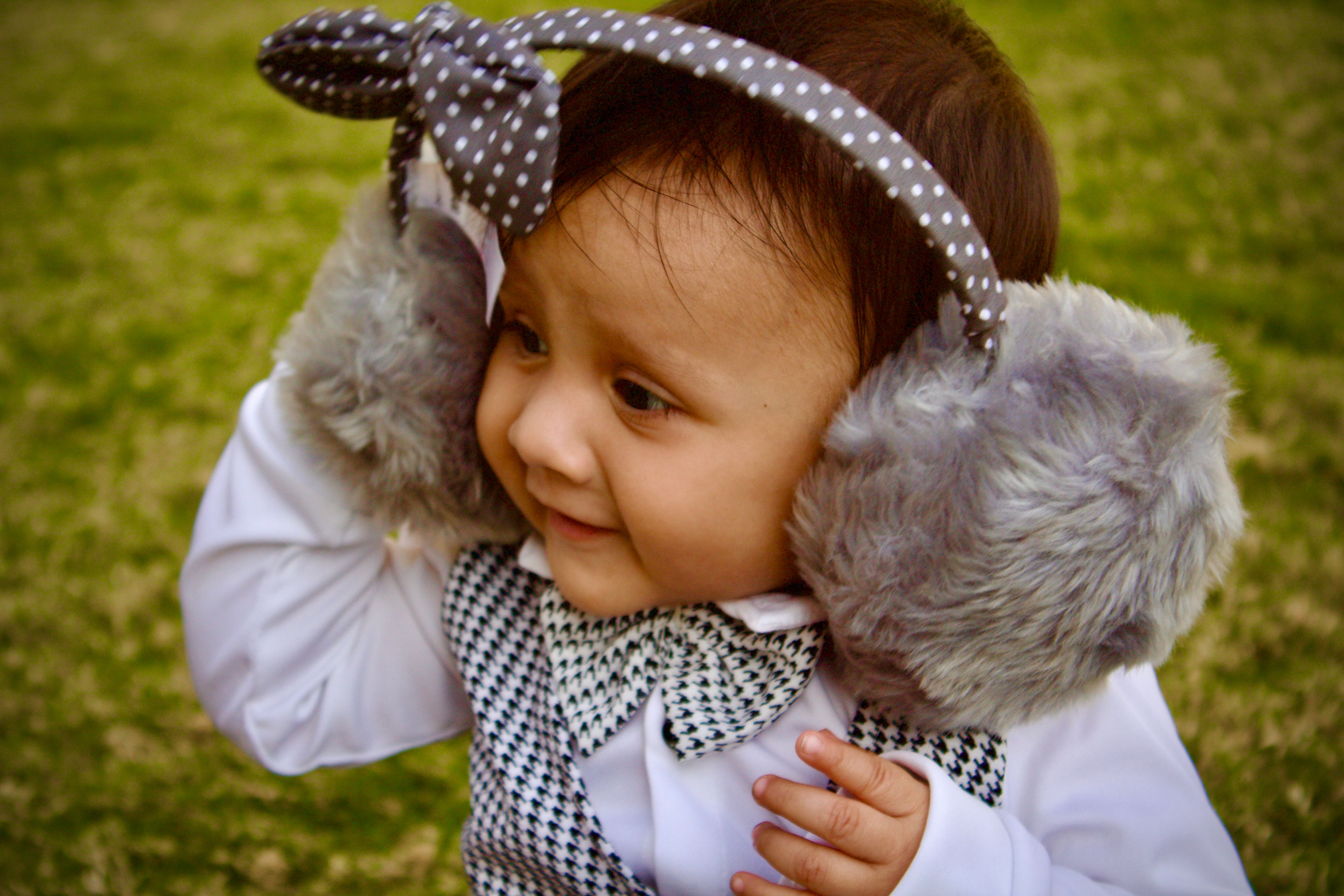 Cute baby boy in stylish outfit wearing earmuffs, enjoying the outdoors.
