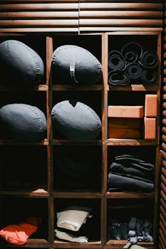 Neatly arranged yoga mats, bolsters, and blocks on rustic wooden shelves in indoor setting.