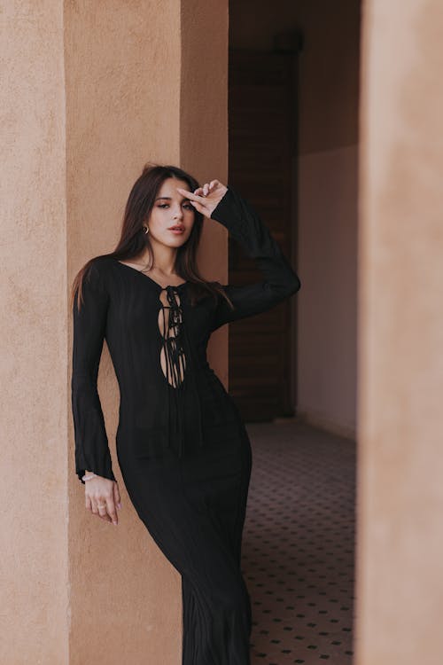 Woman Wearing a Black Dress, Leaning against a Beige Wall
