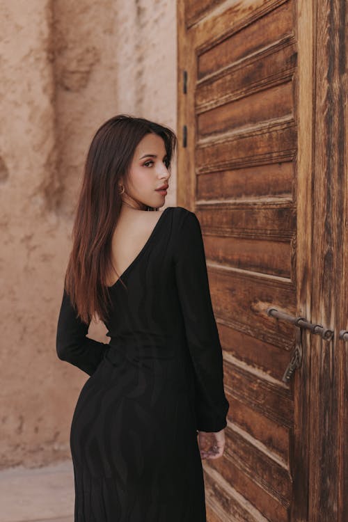 A woman in black dress standing in front of a wooden door