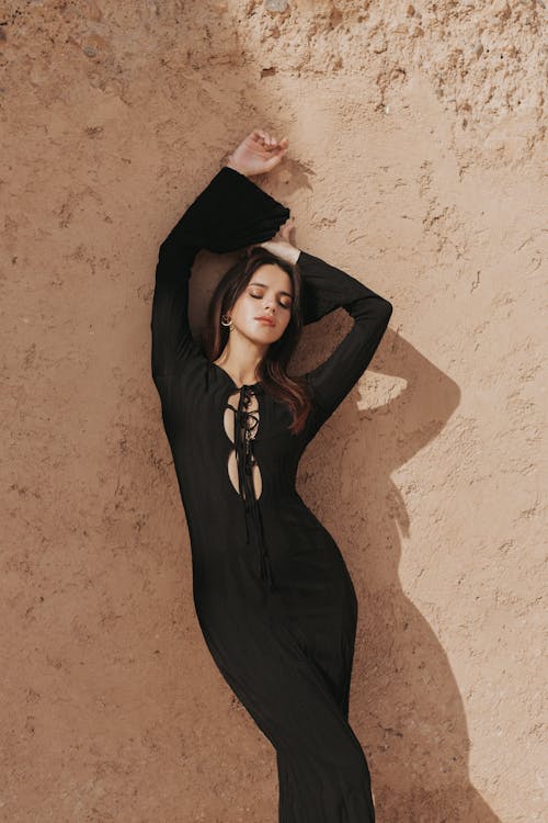 A woman in a black dress poses in front of a wall
