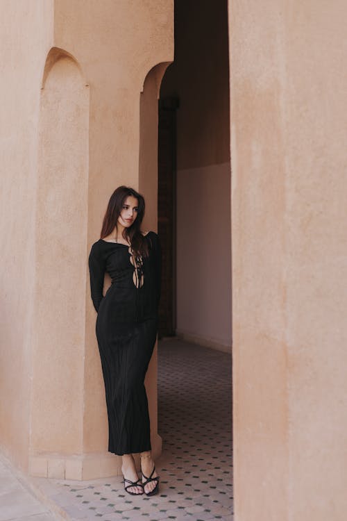 Woman Wearing a Black Dress, Leaning against a Beige Wall, in Marrakesh