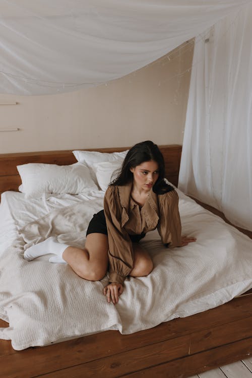Woman in Brown Blouse is Sitting on Bed