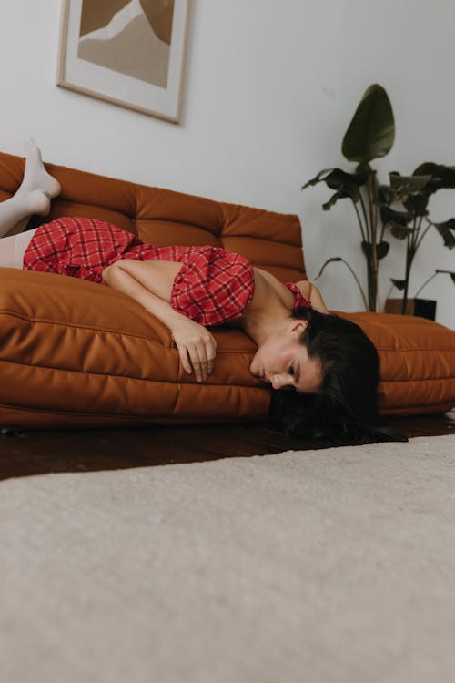 A woman laying on a brown couch with her head in her hands