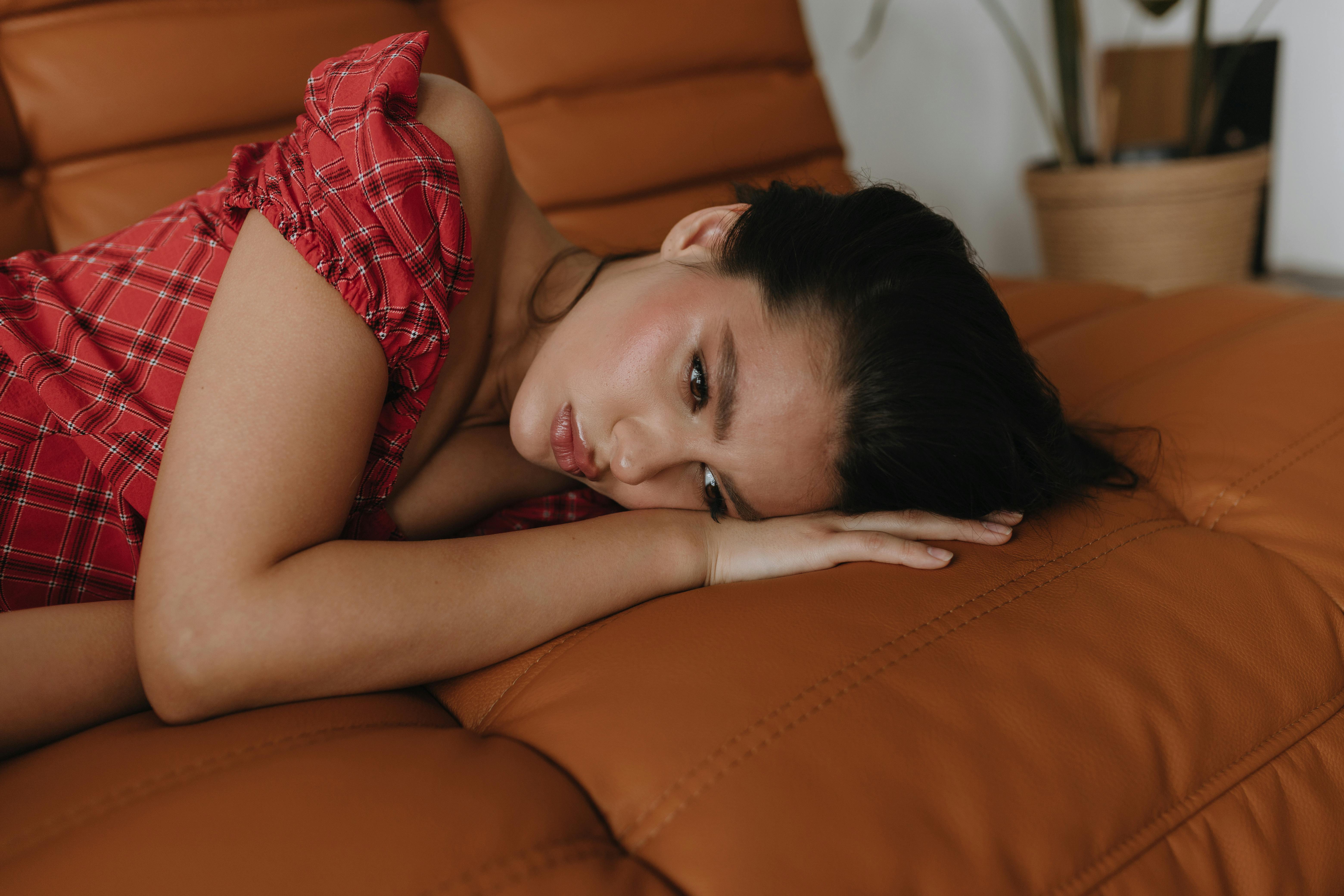 Close-up portrait of a woman in red dress lying on a leather sofa indoors.