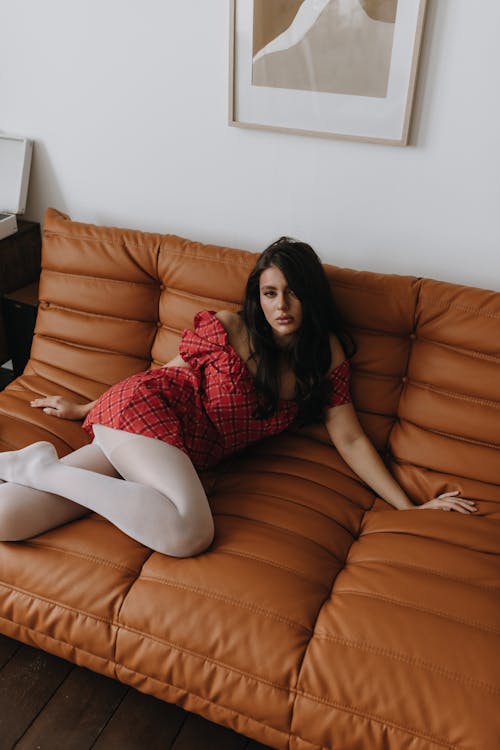 A woman in a red dress sitting on a brown leather couch