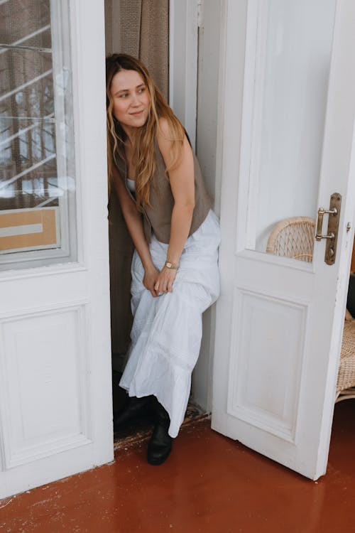 A woman in a white dress is leaning out of a door