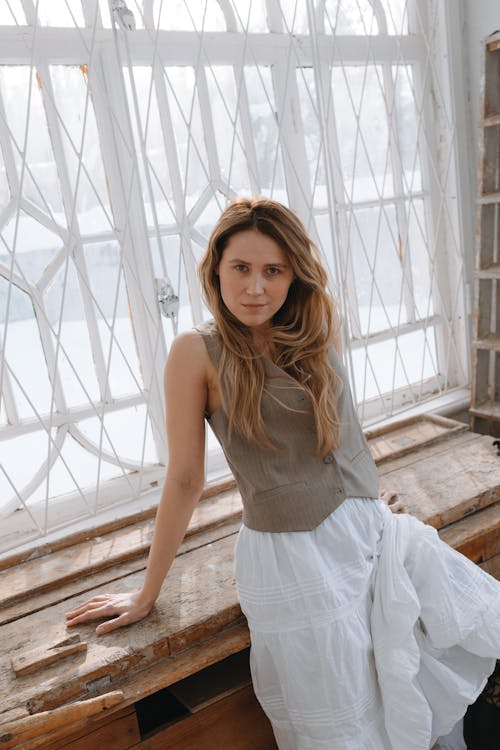 A woman sitting on a window sill in a white dress