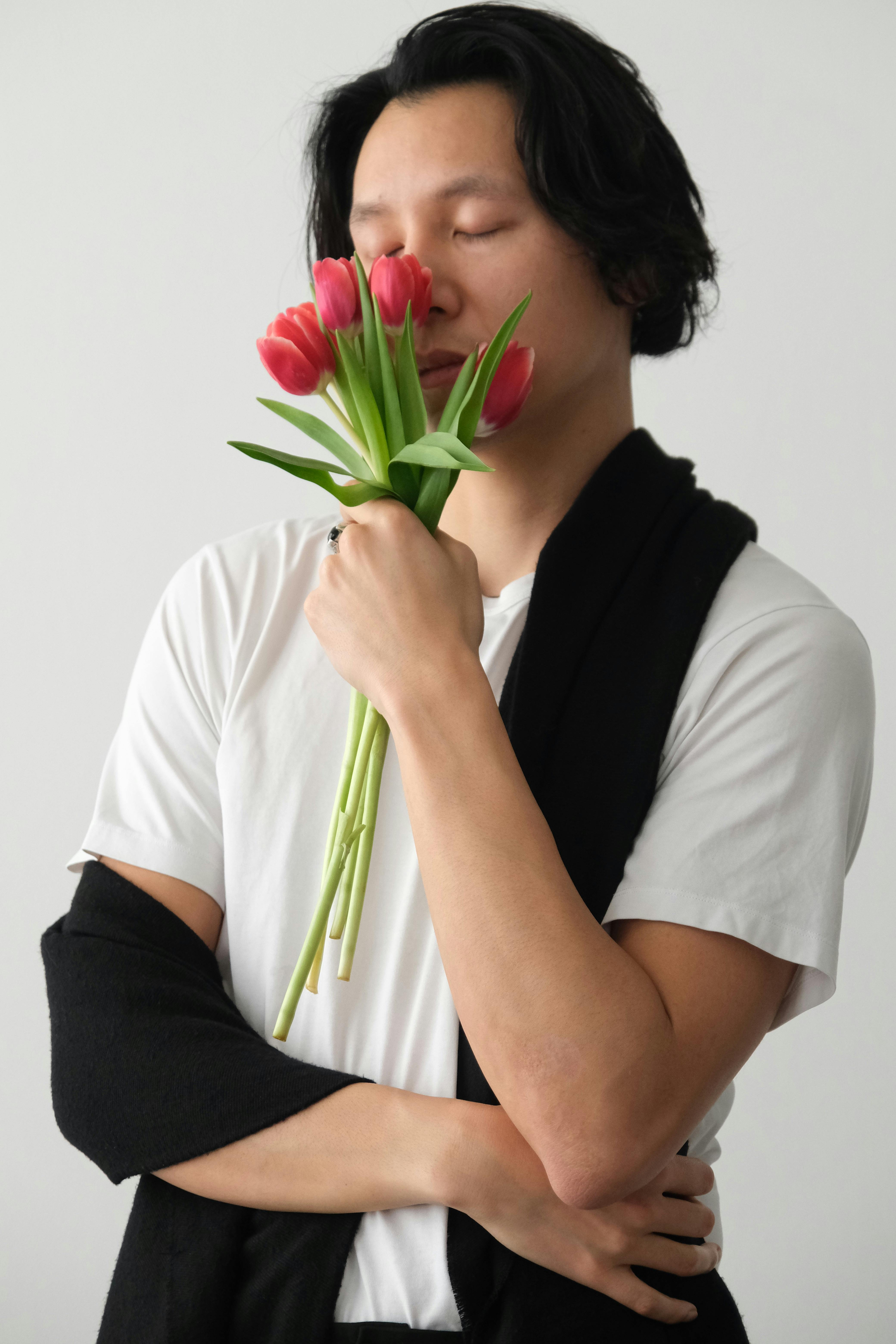Portrait of a serene man with eyes closed, holding a bunch of red tulips indoors.