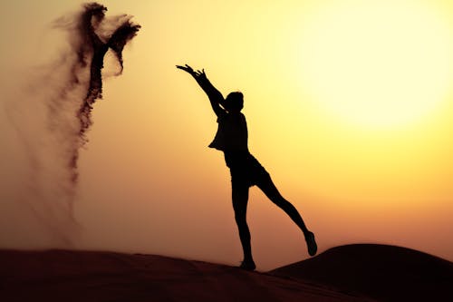 Silhouette of Woman Throwing Sand in Desert