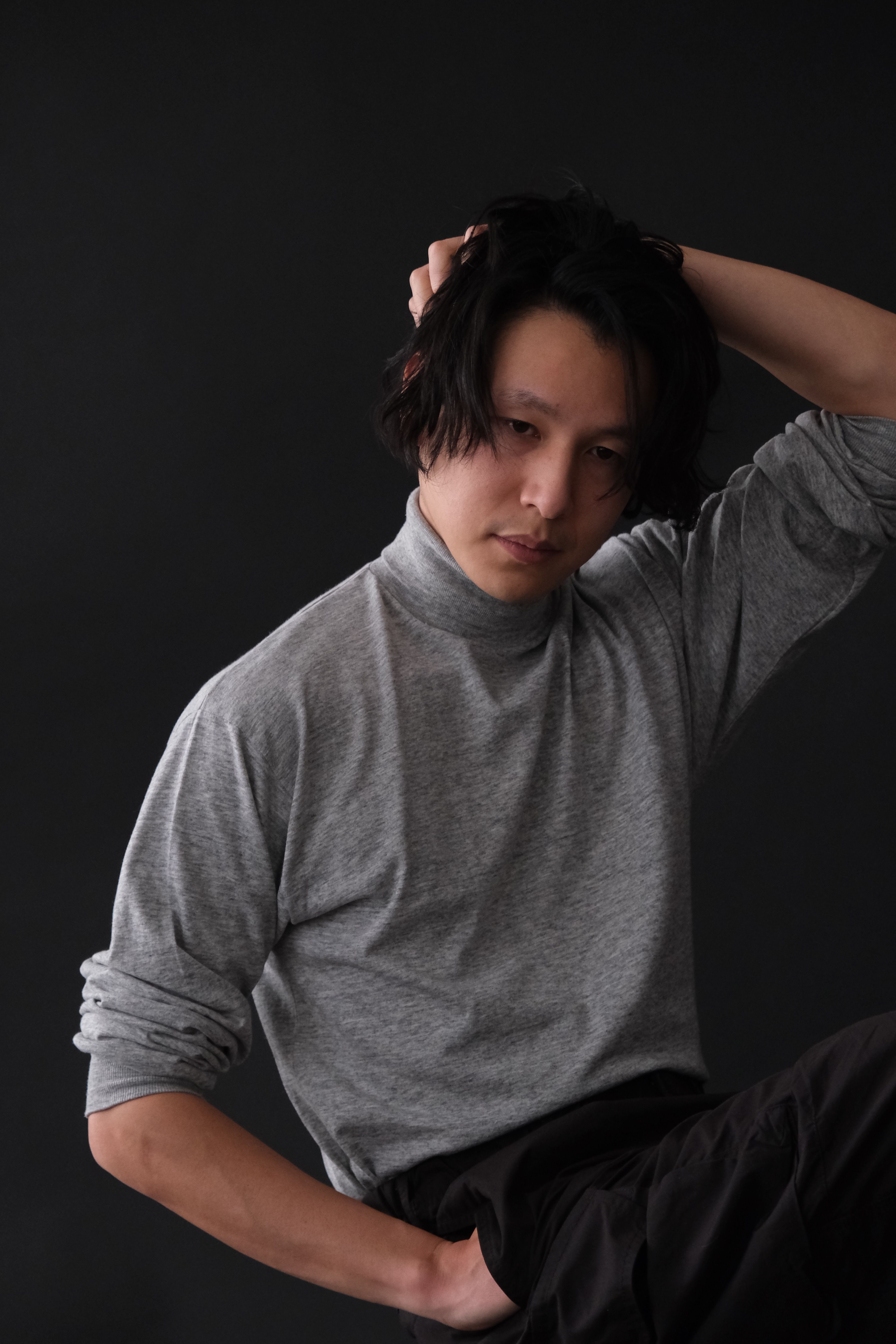 Portrait of an Asian man in a grey turtleneck against a dark backdrop, fashion photography.
