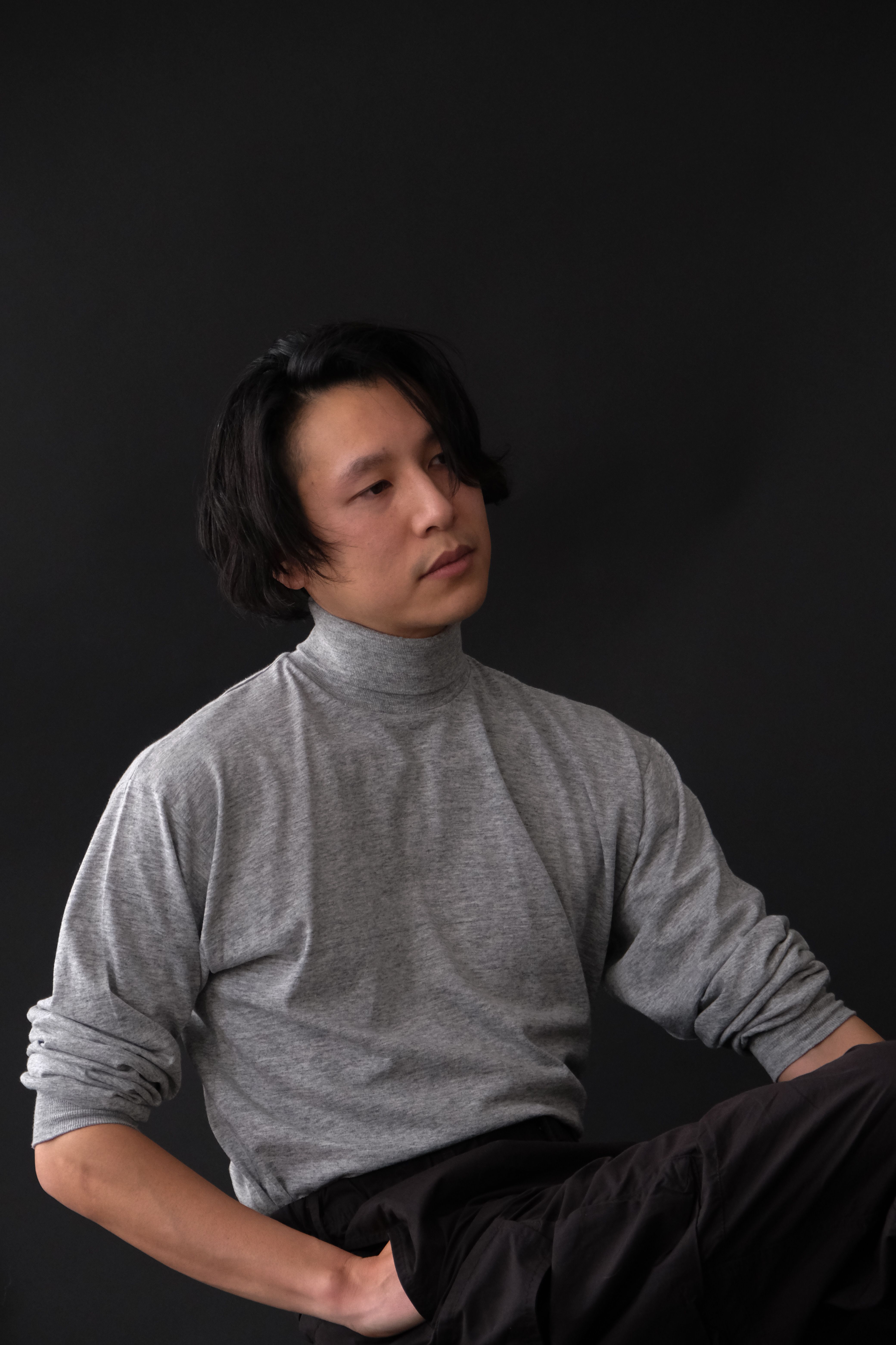 Serene portrait of a man sitting in a gray turtleneck against a dark background.