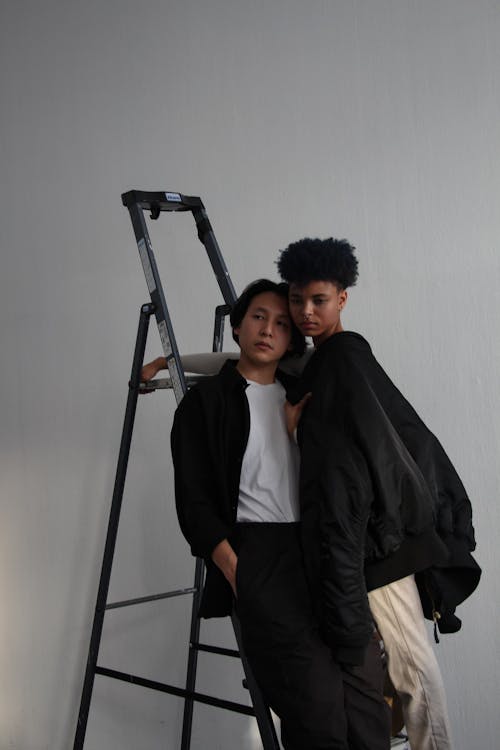 Two people standing on a ladder in front of a white background