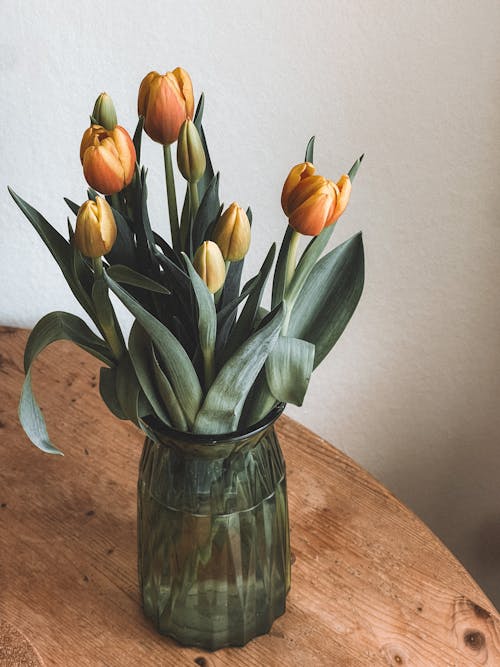 A vase with yellow tulips on top of a wooden table