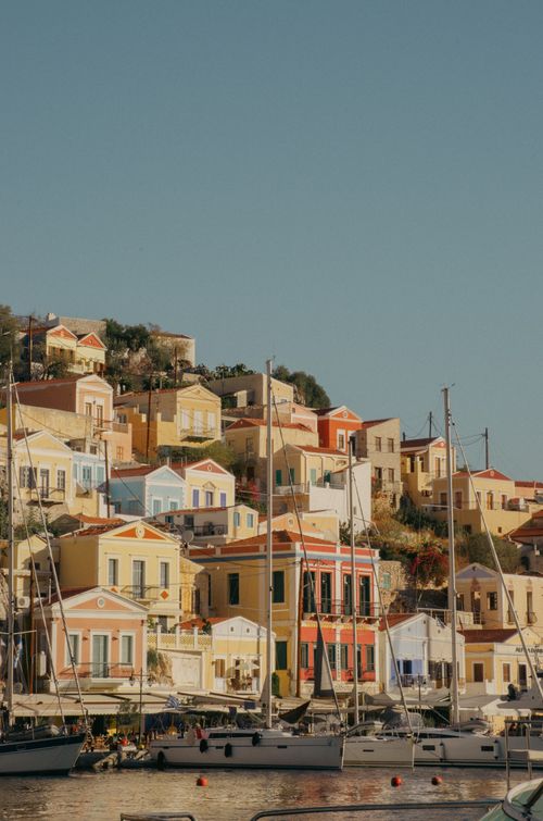Free A picturesque view of a vibrant hillside town in Greece with colorful houses and moored yachts, under a clear sky. Stock Photo