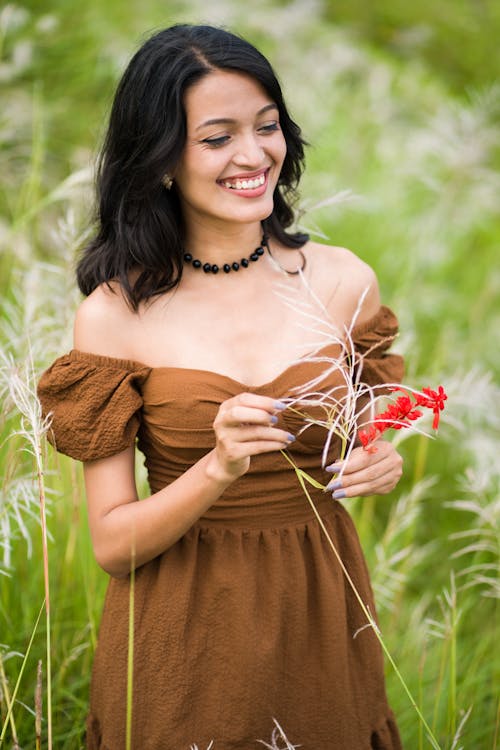 A woman in brown dress holding flowers in tall grass