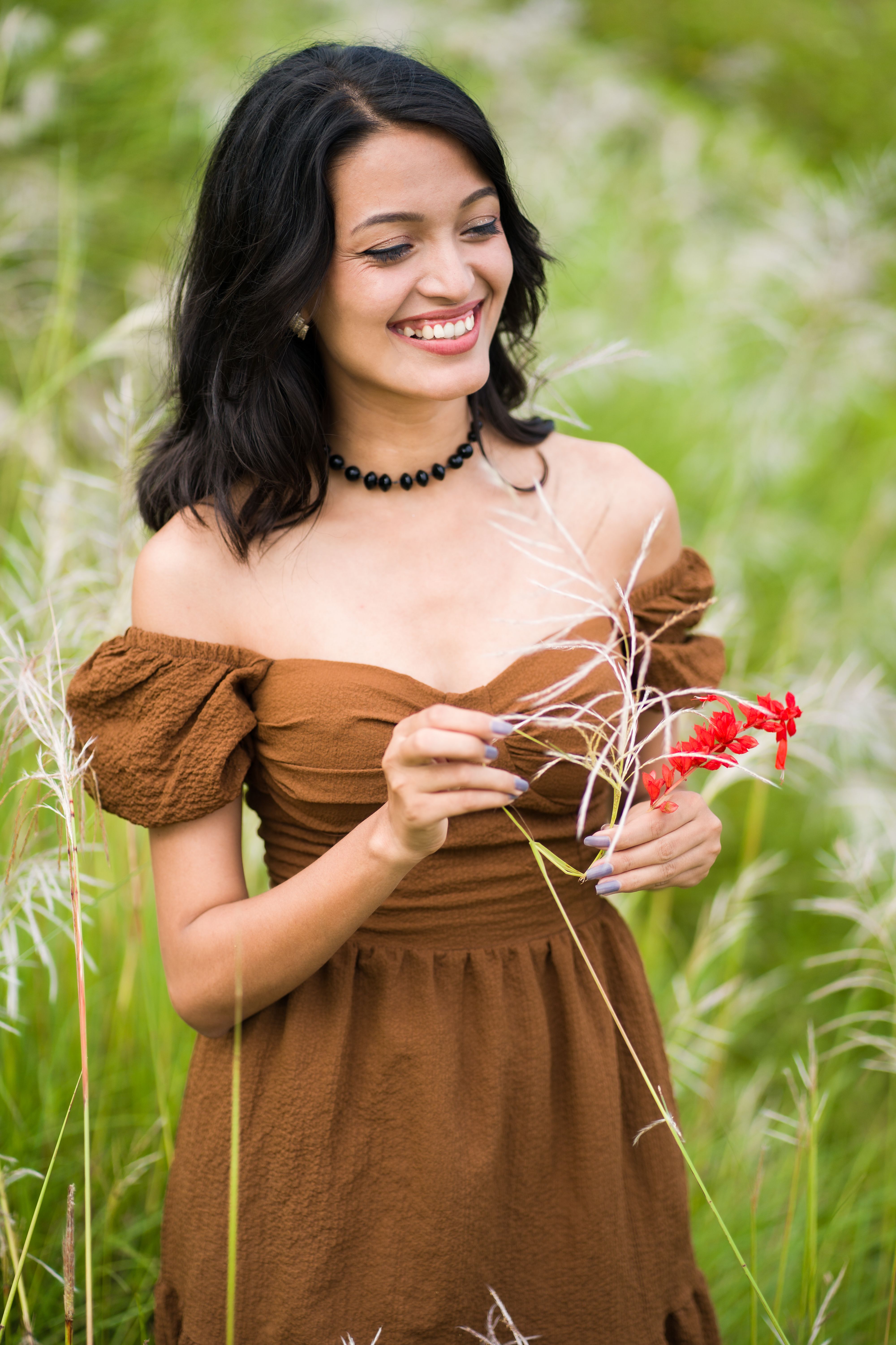 A woman in brown dress holding flowers in tall grass · Free Stock Photo