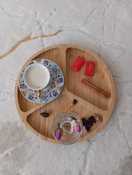 Elegant flat lay of a coffee cup with snacks and floral decoration on a wooden tray, perfect for lifestyle themes.