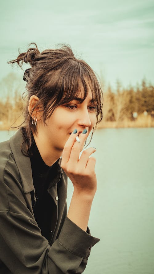 A woman smoking a cigarette by a lake