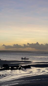 A tranquil coastline scene at sunset featuring a small boat silhouetted against the horizon.