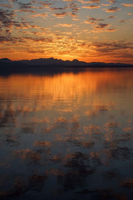 Beautiful sunrise reflecting over Chiemsee Lake with mountains in the distance.