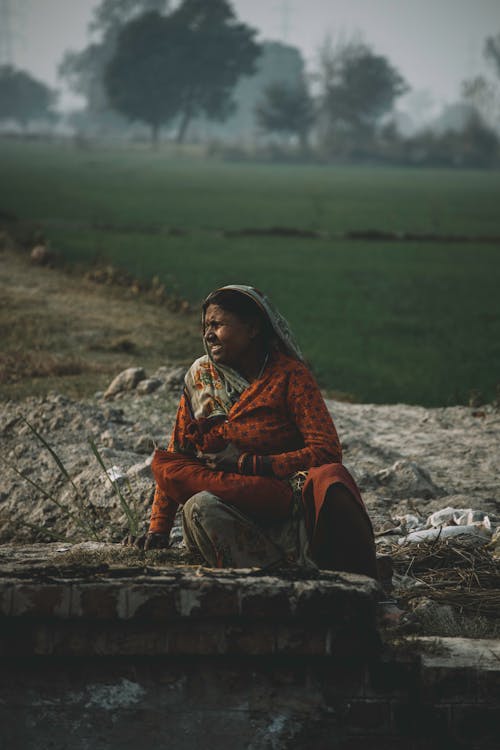 A woman sitting on a brick wall in a field