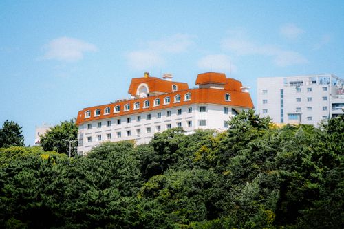 Free A scenic view of a red-roofed building surrounded by lush green trees under a bright blue sky. Stock Photo