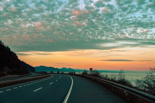 A serene coastal road with mountain views at sunset, perfect for travel inspiration.