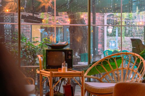 Free Warm and inviting café setting adorned with vintage décor, lush greenery, and cozy seating on a rainy day. Stock Photo
