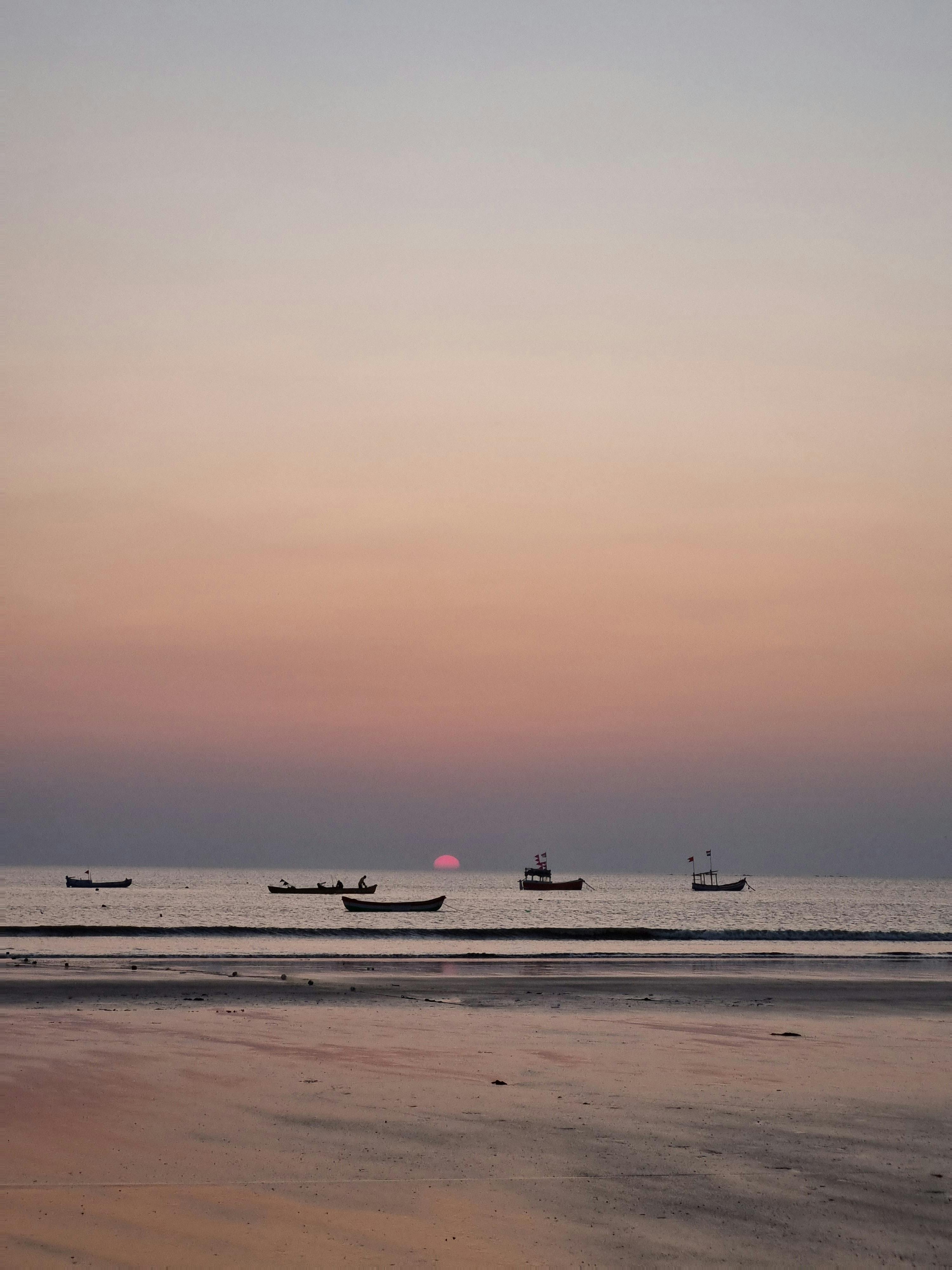 Tranquil sunset over Vasai-Virar beach with boats silhouetted against a pink sky.