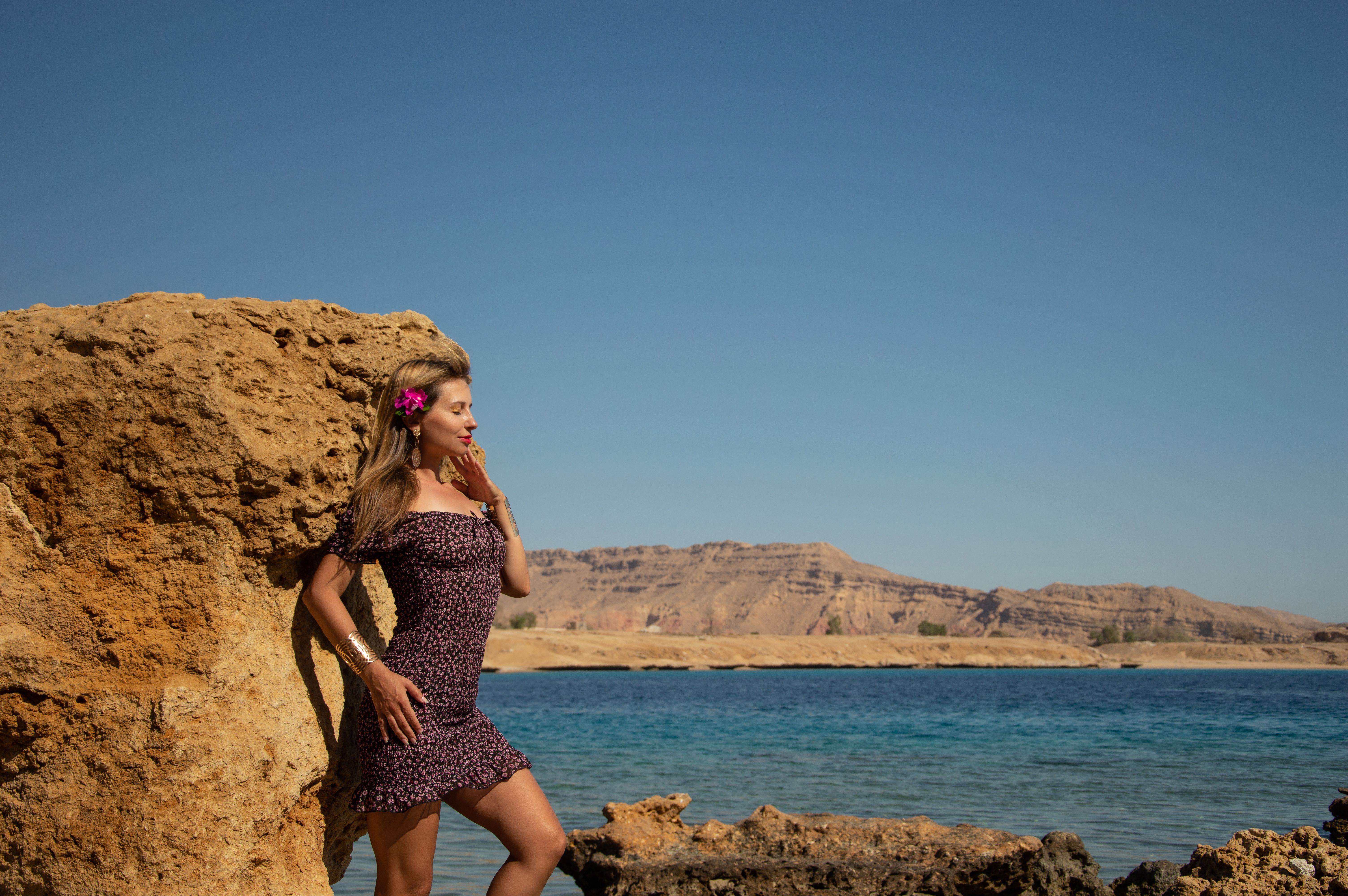 A woman in a dress standing on a rock near the ocean · Free Stock Photo